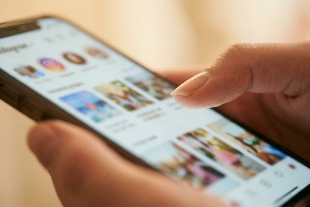 A finger hovering over a blurred social media feed on a phone screen in warm soft light.