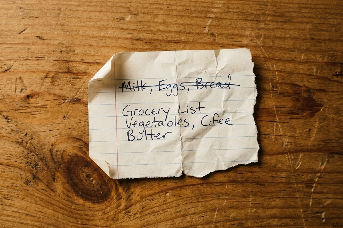 A crumpled handwritten list with one item crossed off resting on a warm wood surface in natural side light.