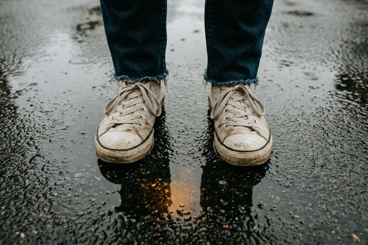 Worn sneakers on wet pavement shot from above after rain, showing up anyway on a hard day.