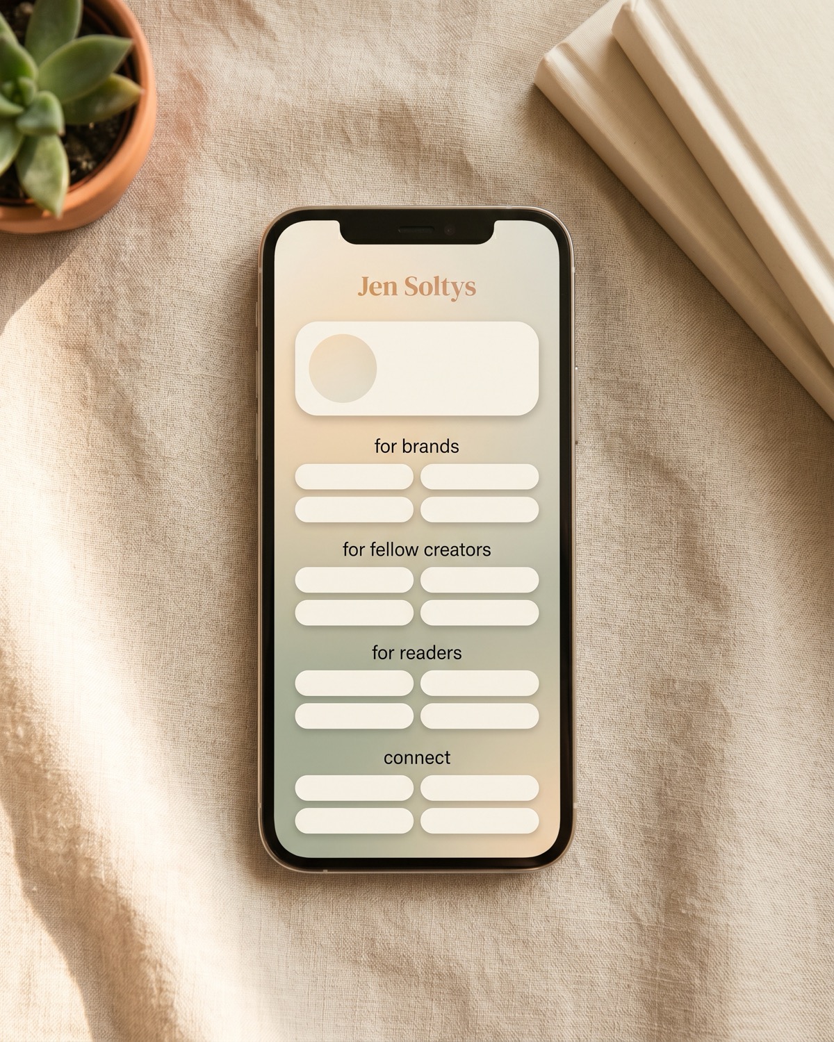 A smartphone on soft sand linen showing Jen Soltys's link in bio page with sections for brands, fellow creators, readers, and connect.

