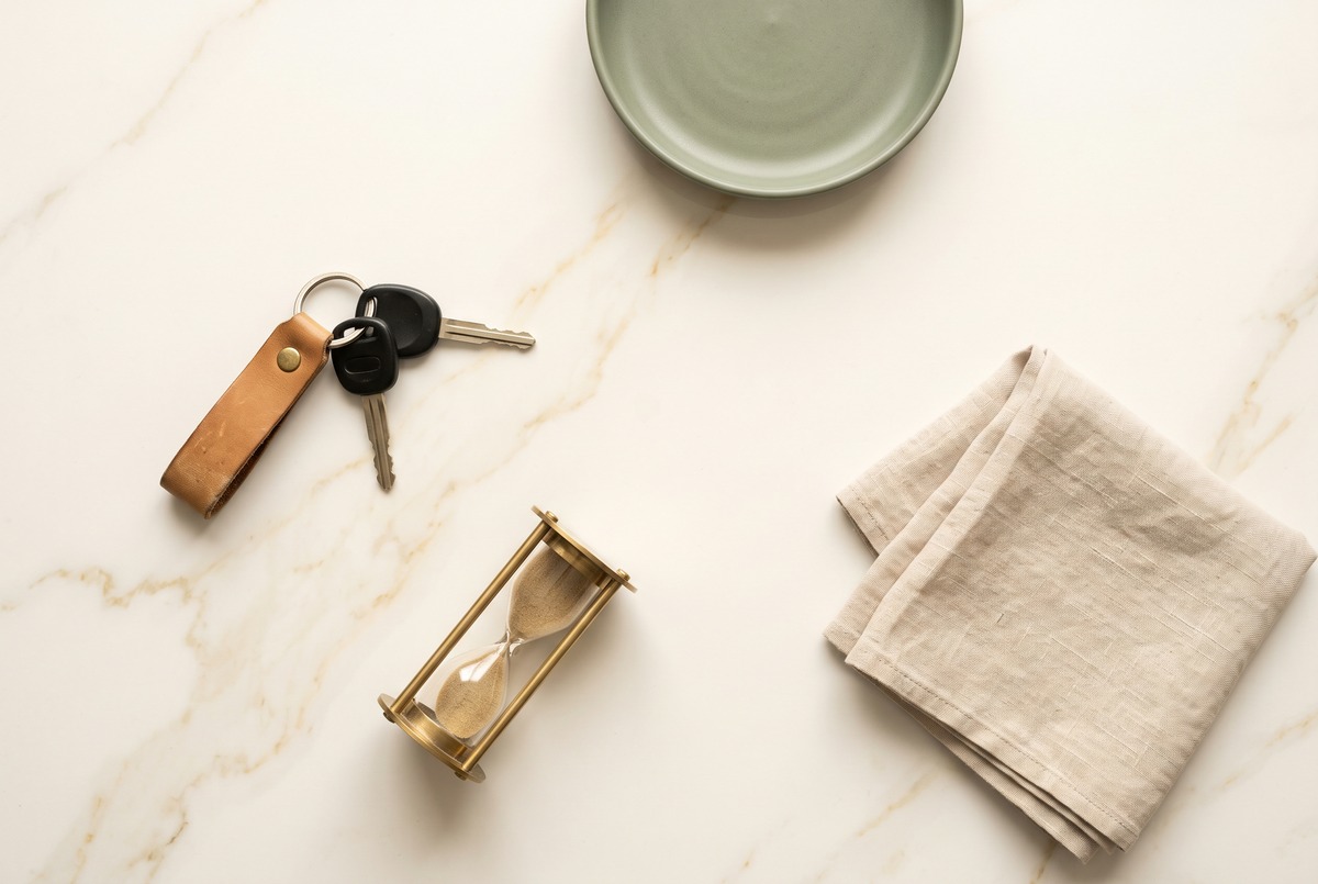Car keys on a leather fob and a small brass hourglass laid out on pale marble, the two side hustle costs that are easiest to forget.